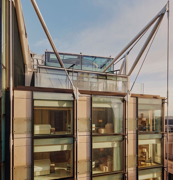 The Emory exterior, with view into suites via full length windows, and sails holding up the building. Blue sky in the background.